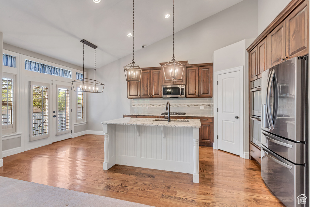 Kitchen featuring backsplash, pendant lighting, light hardwood / wood-style flooring, and appliances with stainless steel finishes