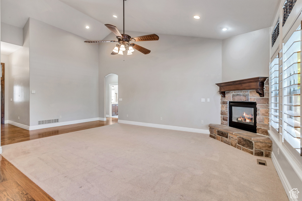 Unfurnished living room featuring high vaulted ceiling, ceiling fan, carpet, and a stone fireplace