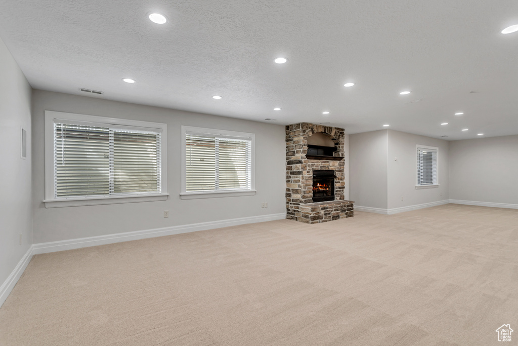 Unfurnished living room with light colored carpet, a textured ceiling, and a stone fireplace