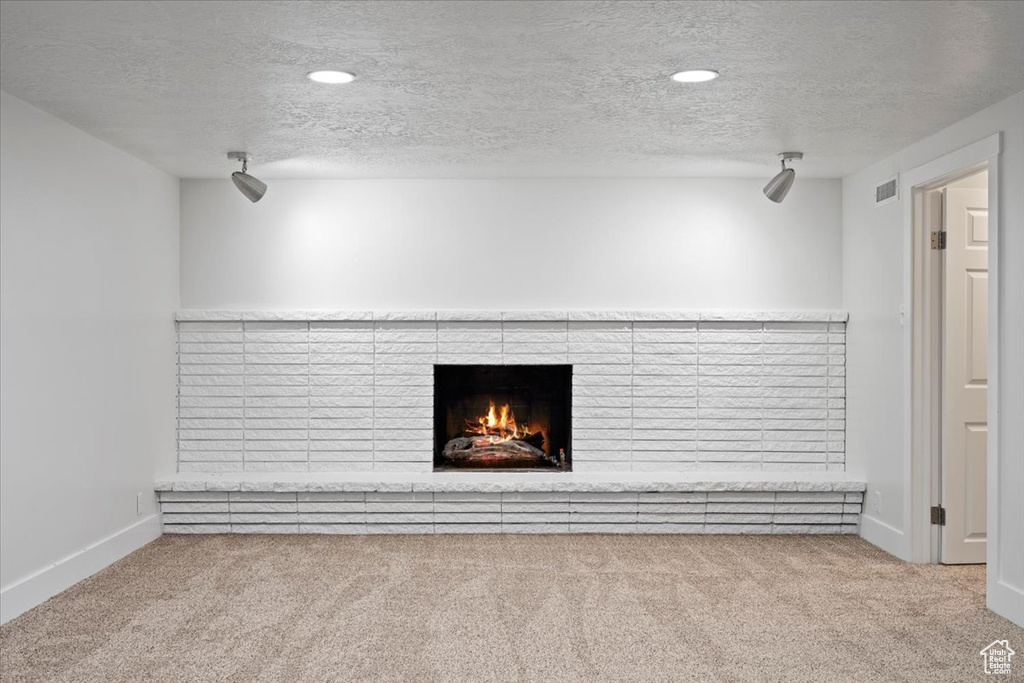 Unfurnished living room with a textured ceiling, light carpet, and a brick fireplace