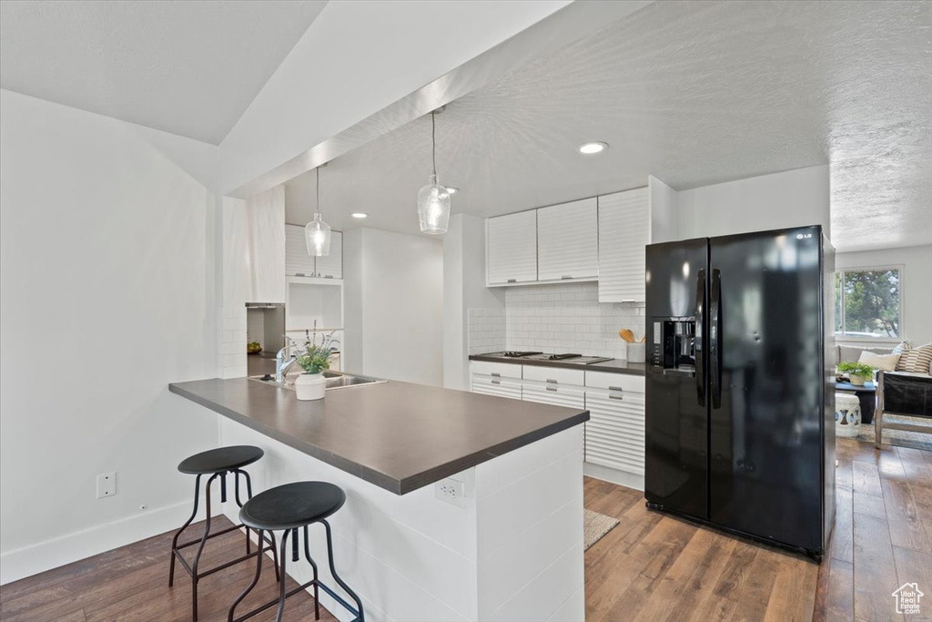 Kitchen featuring dark hardwood / wood-style flooring, backsplash, white cabinetry, and black fridge