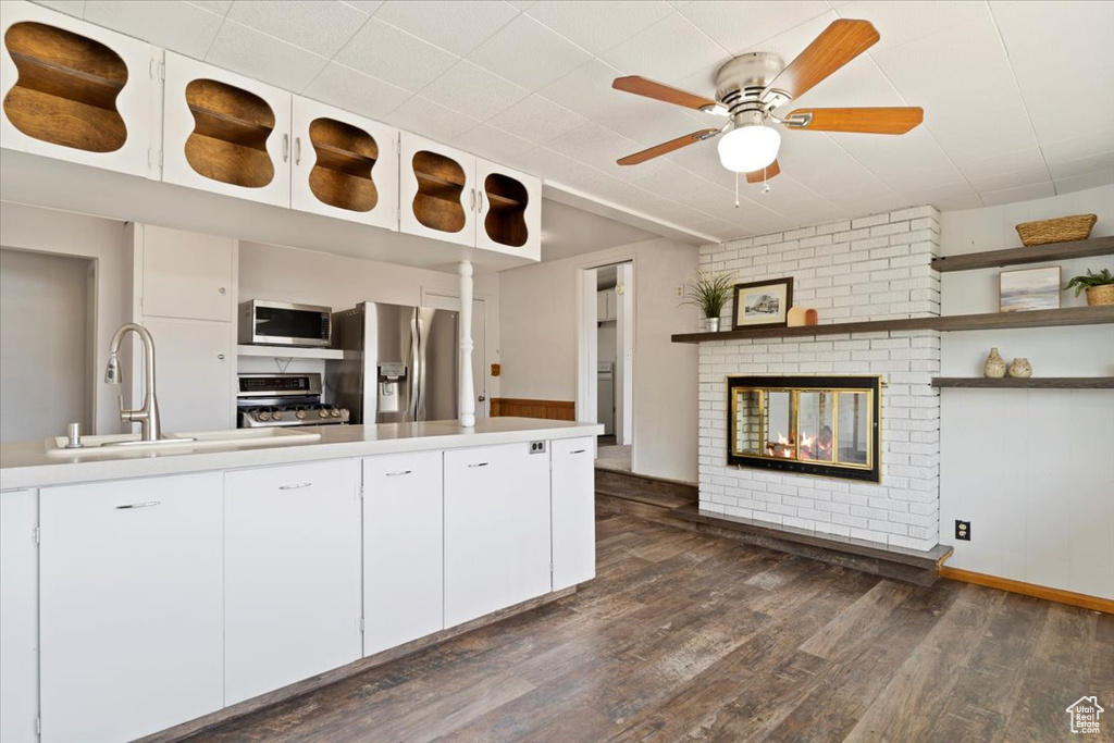 Kitchen featuring ceiling fan, a brick fireplace, white cabinets, dark wood-type flooring, and stainless steel appliances