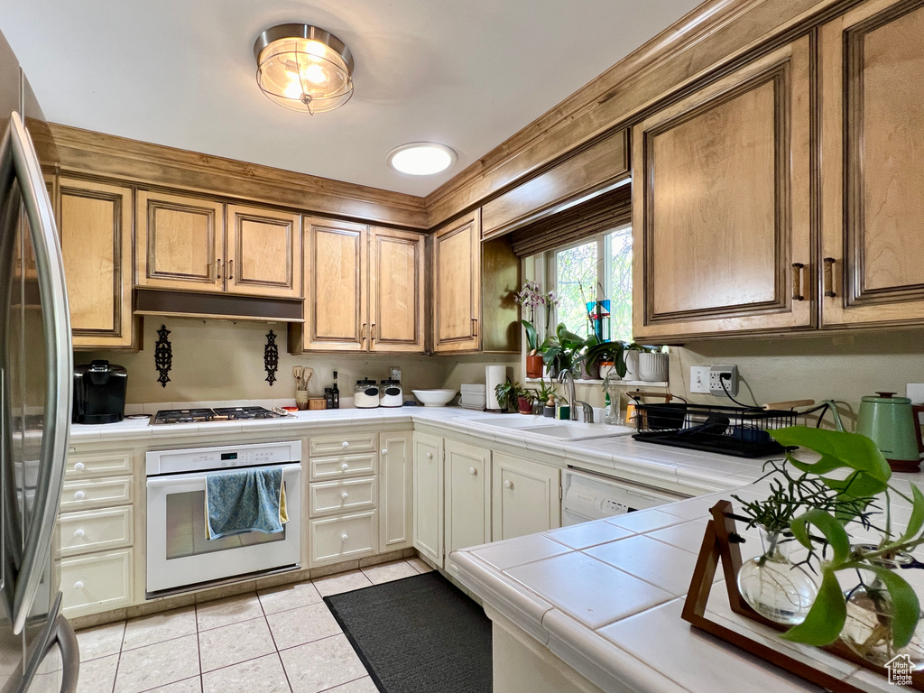 Kitchen with sink, tile countertops, stainless steel appliances, and light tile floors