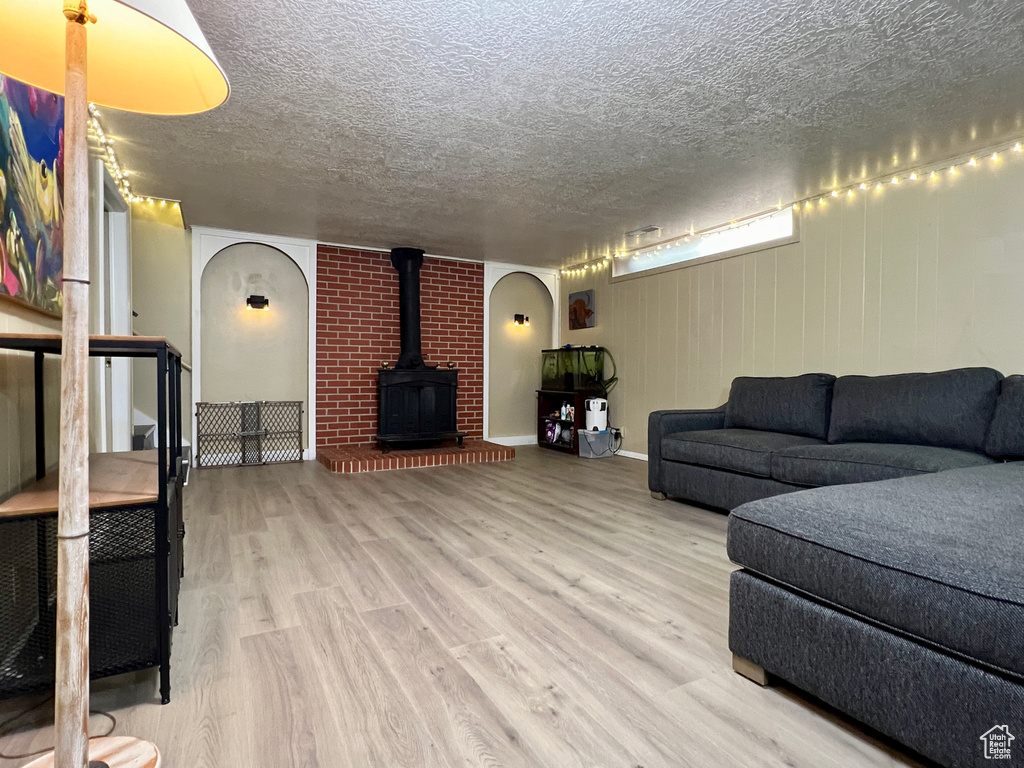 Living room with a textured ceiling, a wood stove, hardwood / wood-style flooring, and brick wall