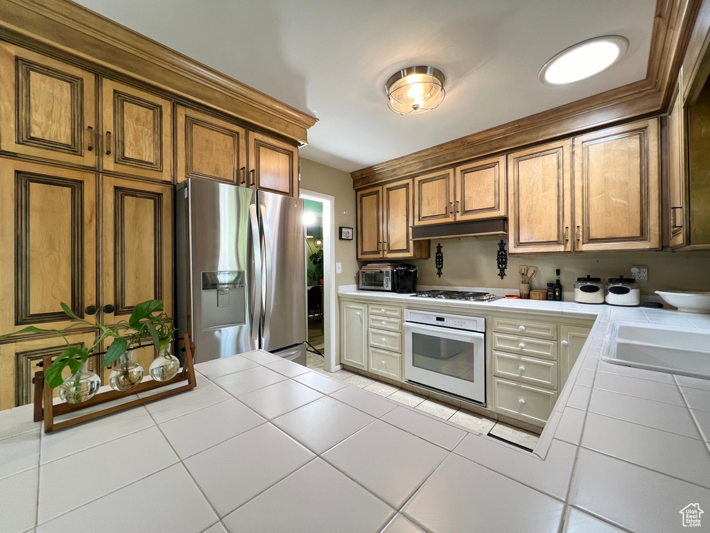 Kitchen featuring tile counters, sink, stainless steel appliances, and light tile floors