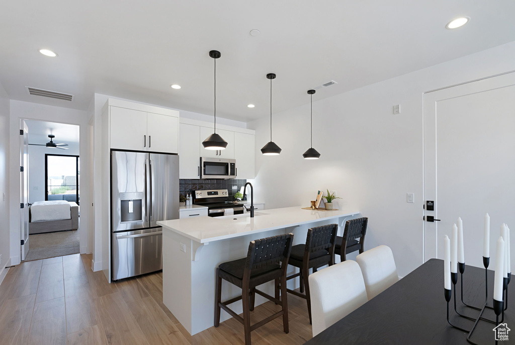 Kitchen with pendant lighting, stainless steel appliances, ceiling fan, light wood-type flooring, and white cabinets