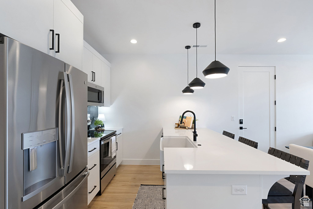 Kitchen with a breakfast bar area, appliances with stainless steel finishes, hanging light fixtures, white cabinetry, and light wood-type flooring