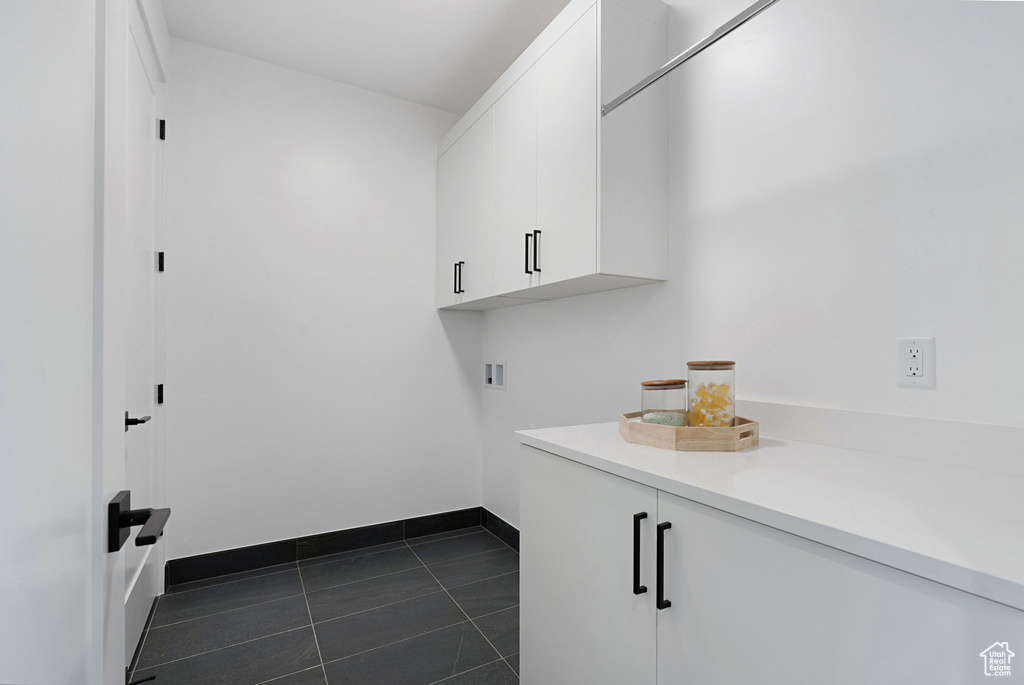 Laundry area with dark tile patterned flooring, hookup for a washing machine, and cabinets