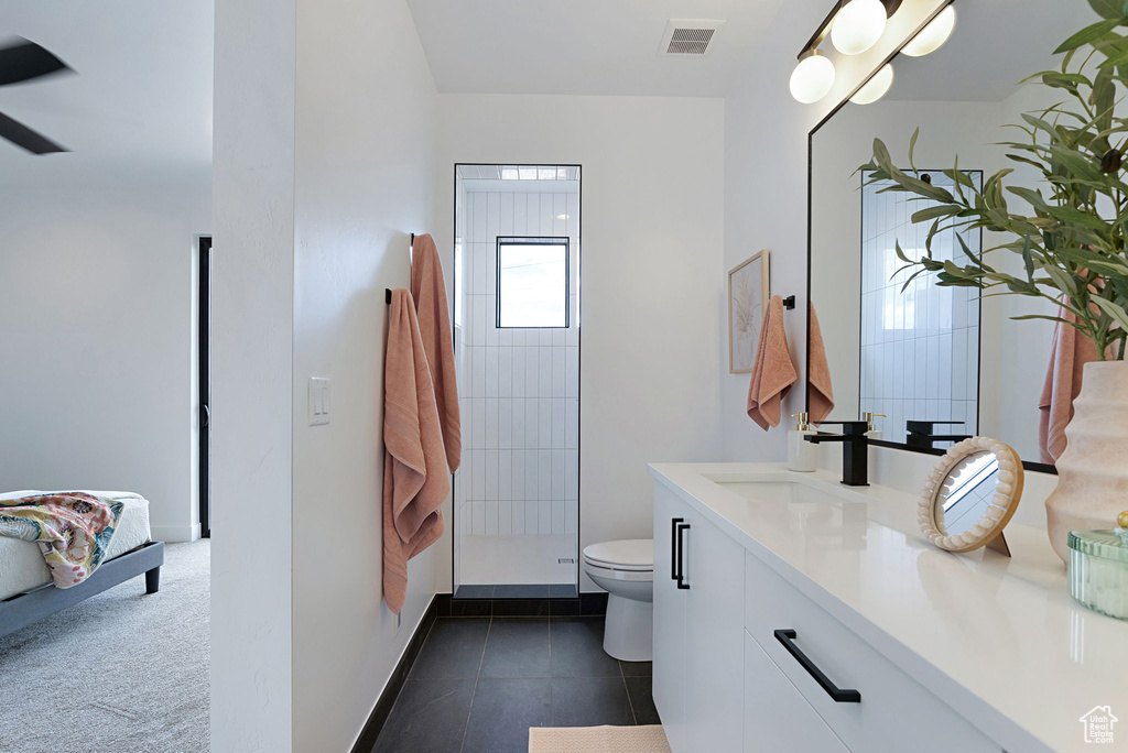 Bathroom with tiled shower, tile patterned flooring, toilet, and vanity