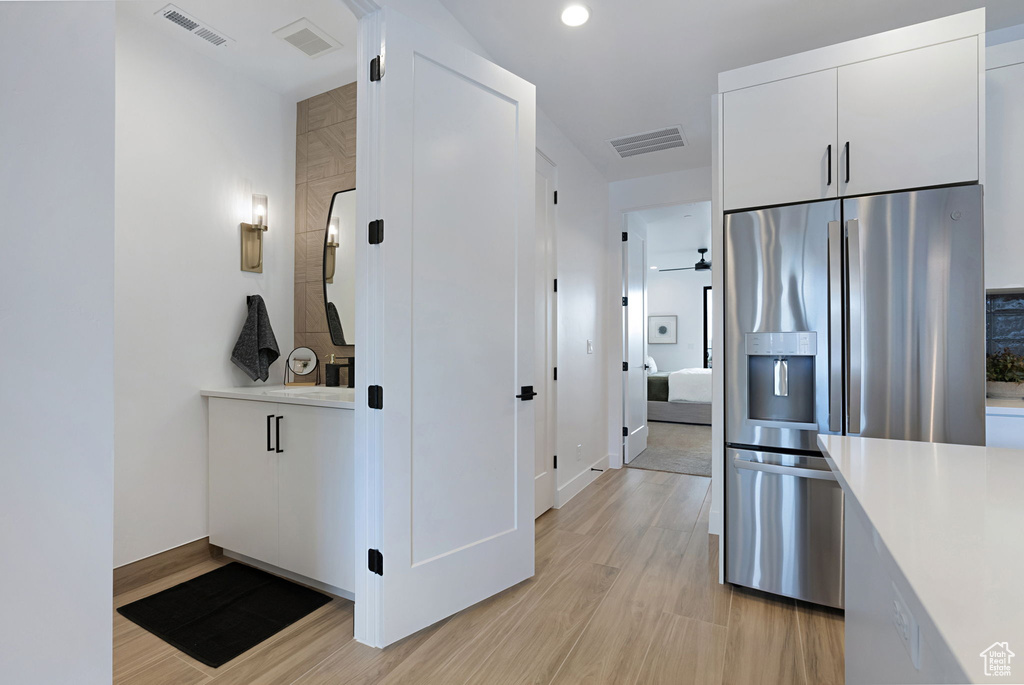 Kitchen with stainless steel fridge with ice dispenser, white cabinetry, light hardwood / wood-style flooring, and stacked washer / drying machine