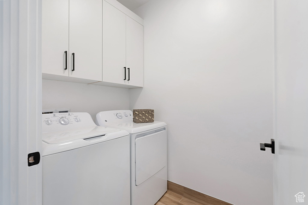 Laundry room featuring separate washer and dryer, cabinets, and light hardwood / wood-style flooring