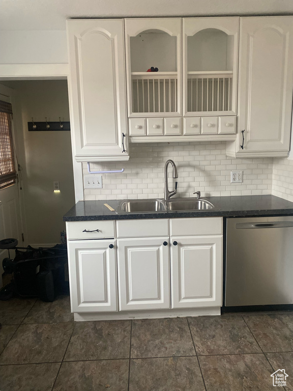 Kitchen featuring stainless steel dishwasher, sink, dark tile flooring, and white cabinets