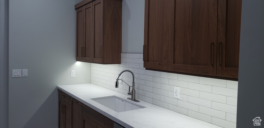 Kitchen featuring tasteful backsplash, dark brown cabinetry, sink, and light stone countertops