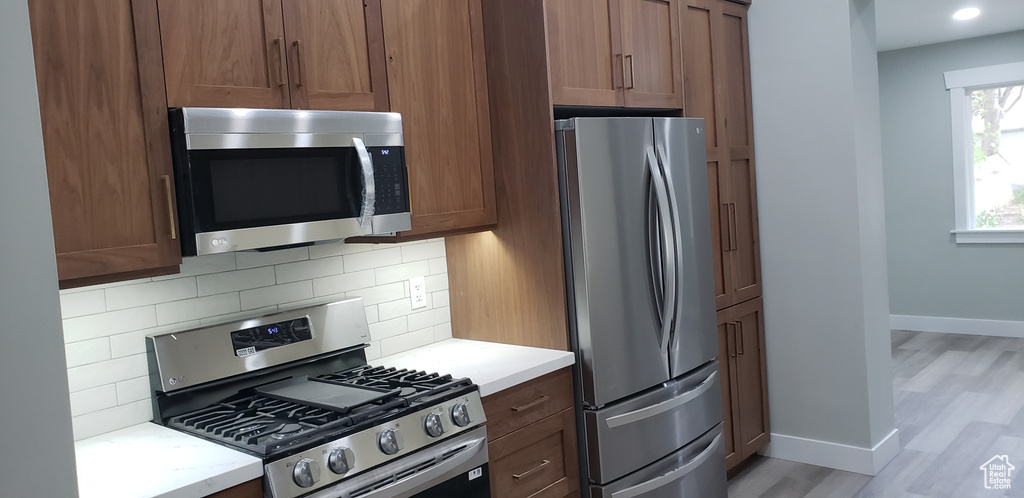 Kitchen with tasteful backsplash, appliances with stainless steel finishes, and wood-type flooring