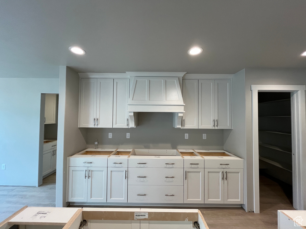 Kitchen featuring white cabinets, light wood-type flooring, and premium range hood