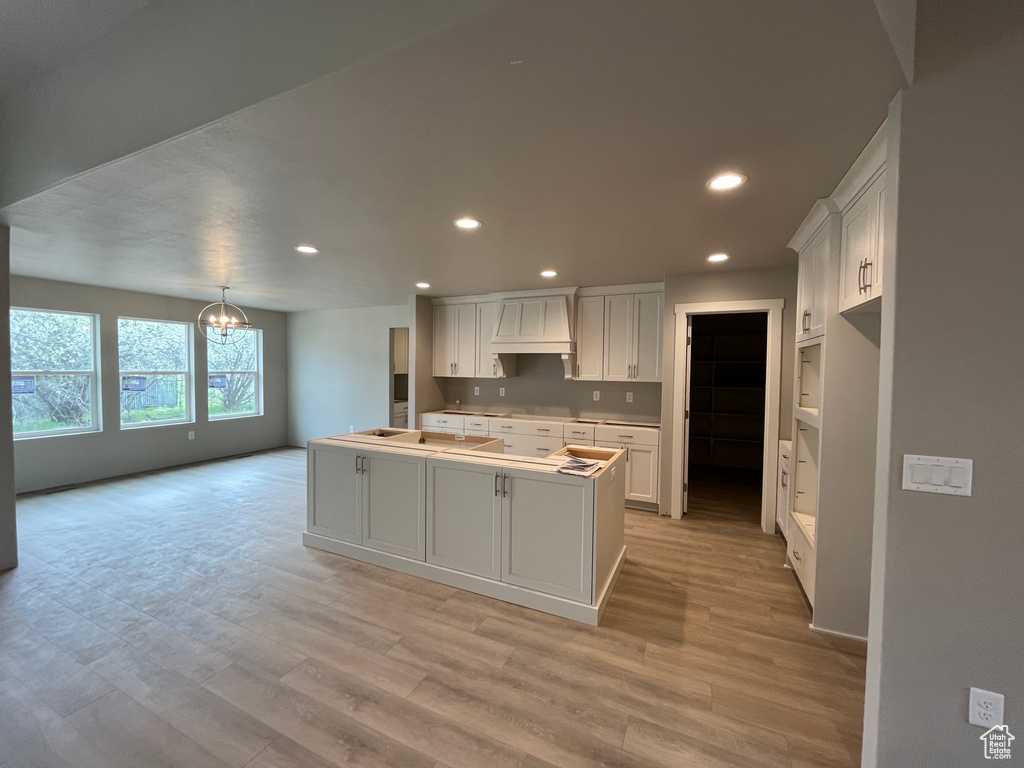 Kitchen featuring light hardwood / wood-style floors, a center island with sink, custom exhaust hood, and white cabinetry
