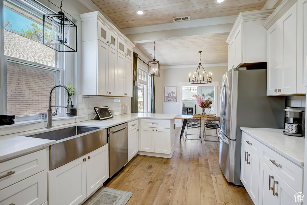 Kitchen with decorative light fixtures, light hardwood / wood-style flooring, white cabinetry, appliances with stainless steel finishes, and tasteful backsplash