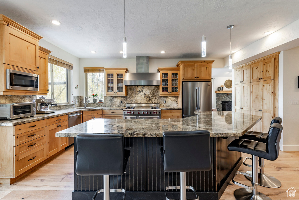 Kitchen featuring appliances with stainless steel finishes, a breakfast bar, wall chimney exhaust hood, and a large island