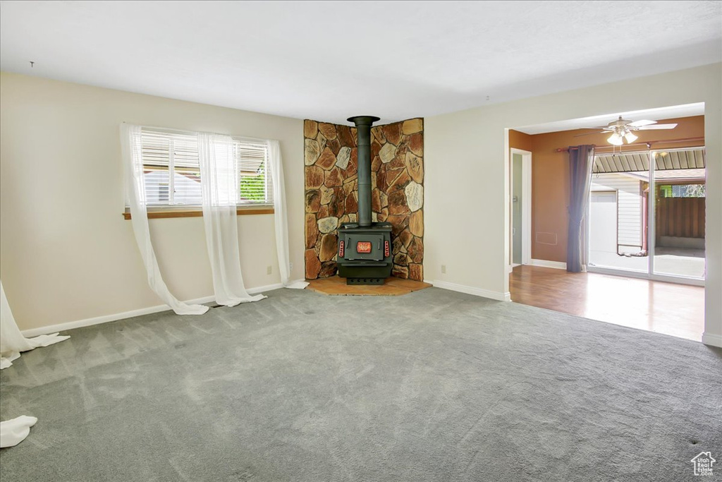 Unfurnished living room featuring a wood stove, ceiling fan, and carpet