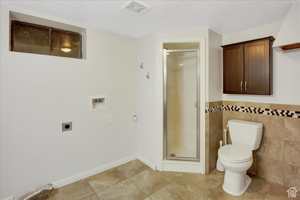 Bathroom featuring tile floors, tile walls, a shower with shower door, toilet, and a textured ceiling