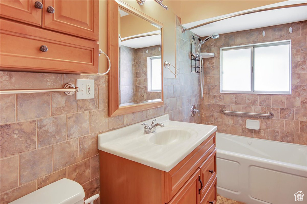 Full bathroom with tiled shower / bath combo, vanity, toilet, and tile walls