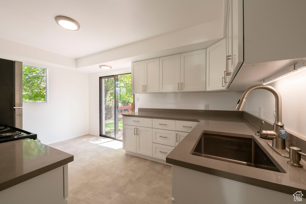 Kitchen with light tile floors, sink, stainless steel refrigerator, white cabinetry, and range with electric stovetop