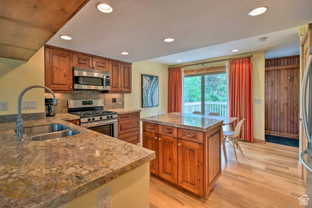 Kitchen with appliances with stainless steel finishes, backsplash, light stone counters, sink, and light wood-type flooring