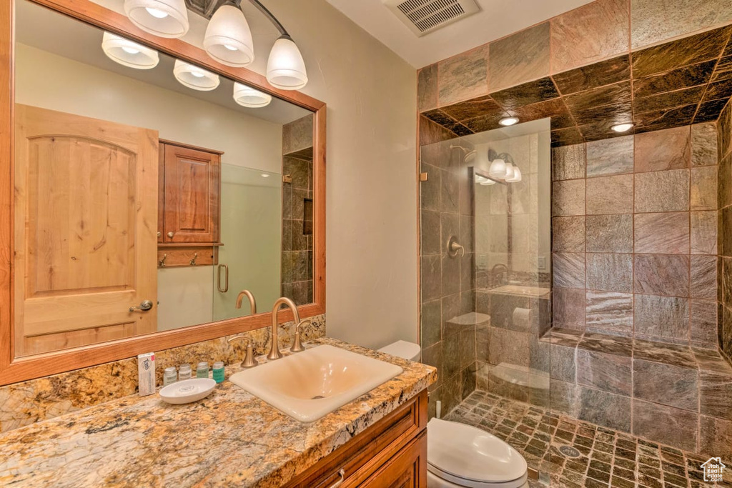 Bathroom featuring vanity with extensive cabinet space, toilet, and a shower with door