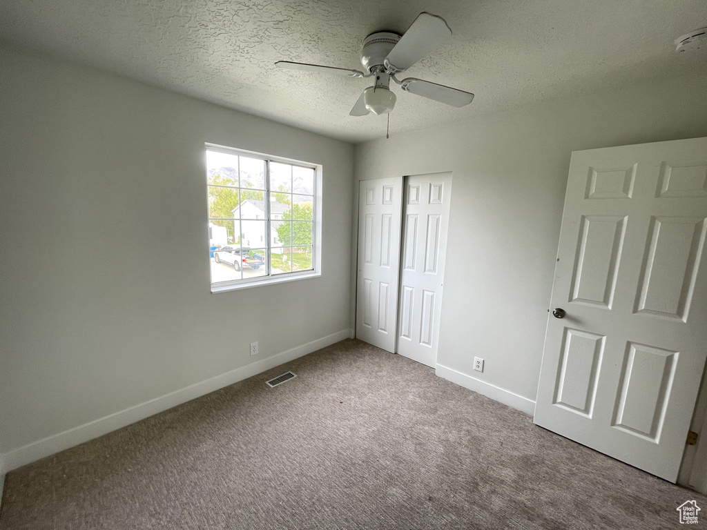 Unfurnished bedroom featuring a closet, a textured ceiling, ceiling fan, and carpet flooring