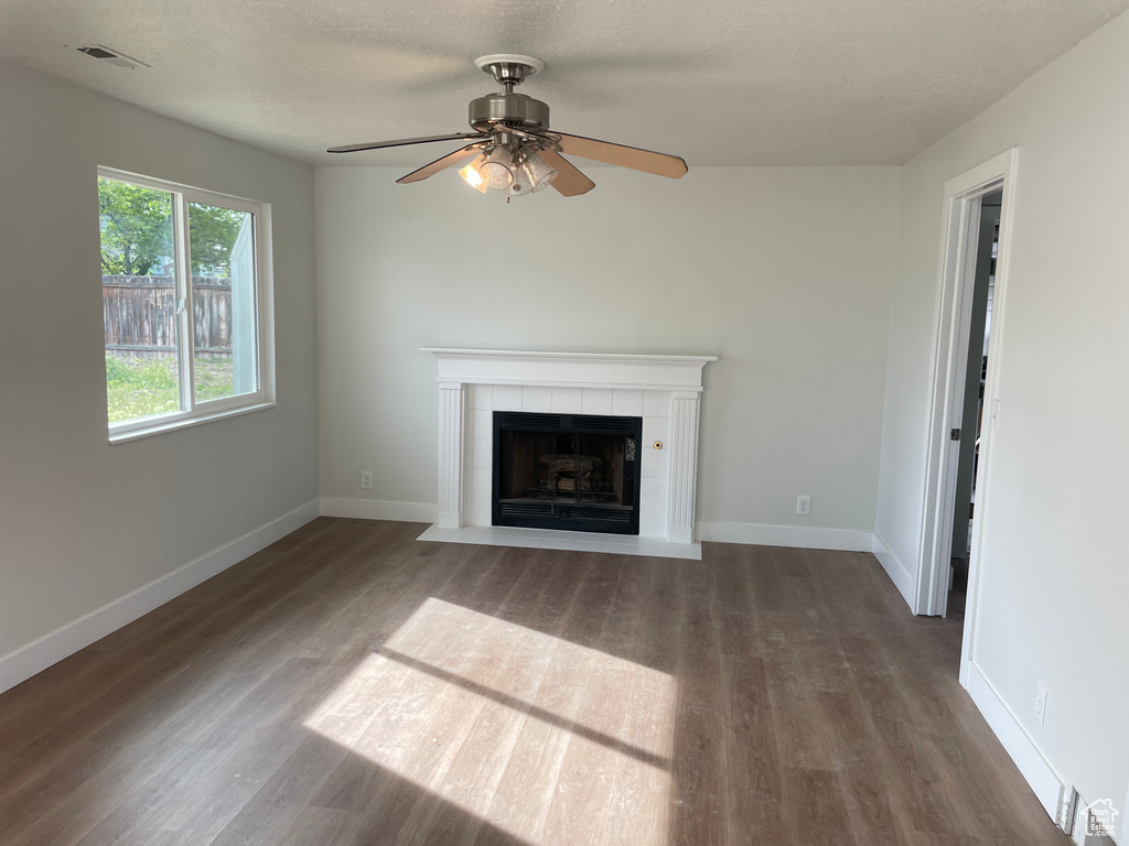 Unfurnished living room with wood-type flooring, ceiling fan, and a tile fireplace