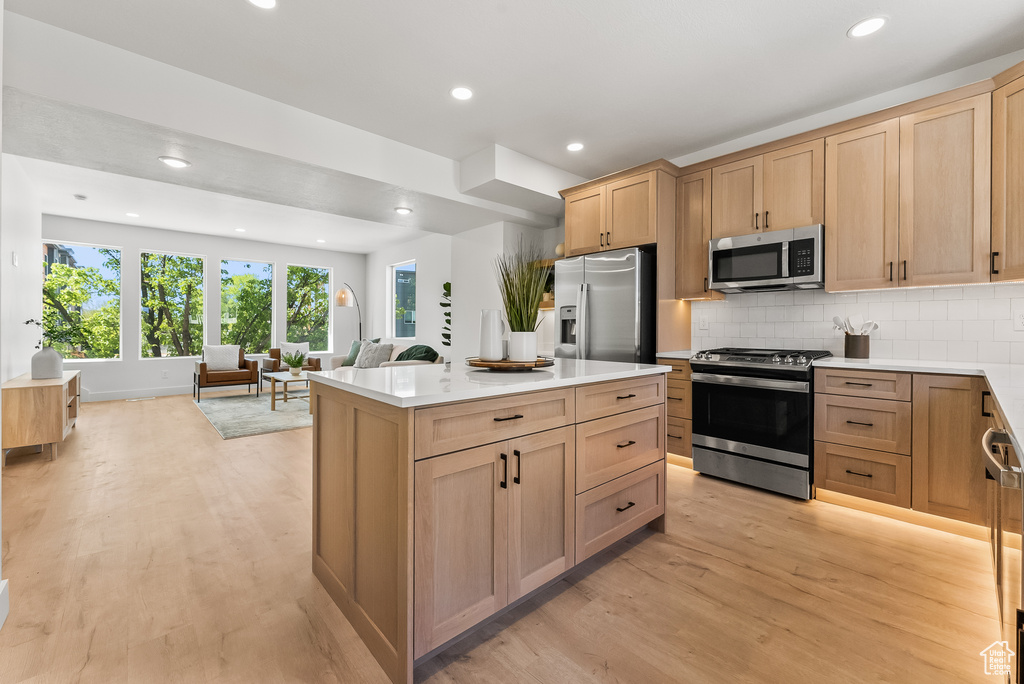 Kitchen featuring light brown cabinets, a center island, tasteful backsplash, light wood-type flooring, and stainless steel appliances