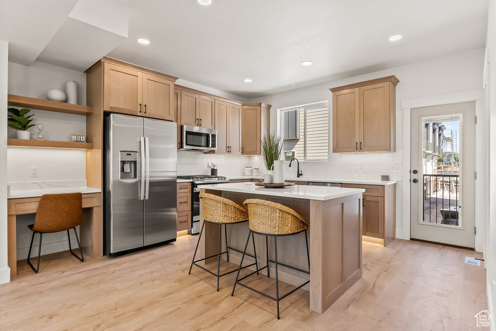 Kitchen with a center island, light wood-type flooring, stainless steel appliances, a breakfast bar area, and tasteful backsplash