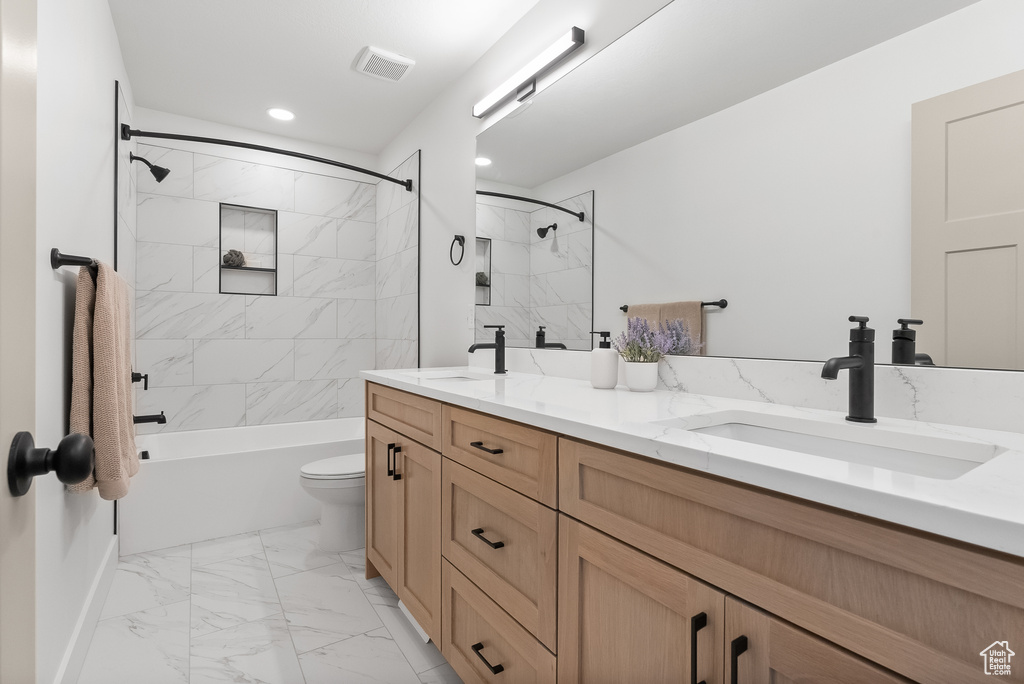 Full bathroom with vanity with extensive cabinet space, tiled shower / bath combo, dual sinks, toilet, and tile floors