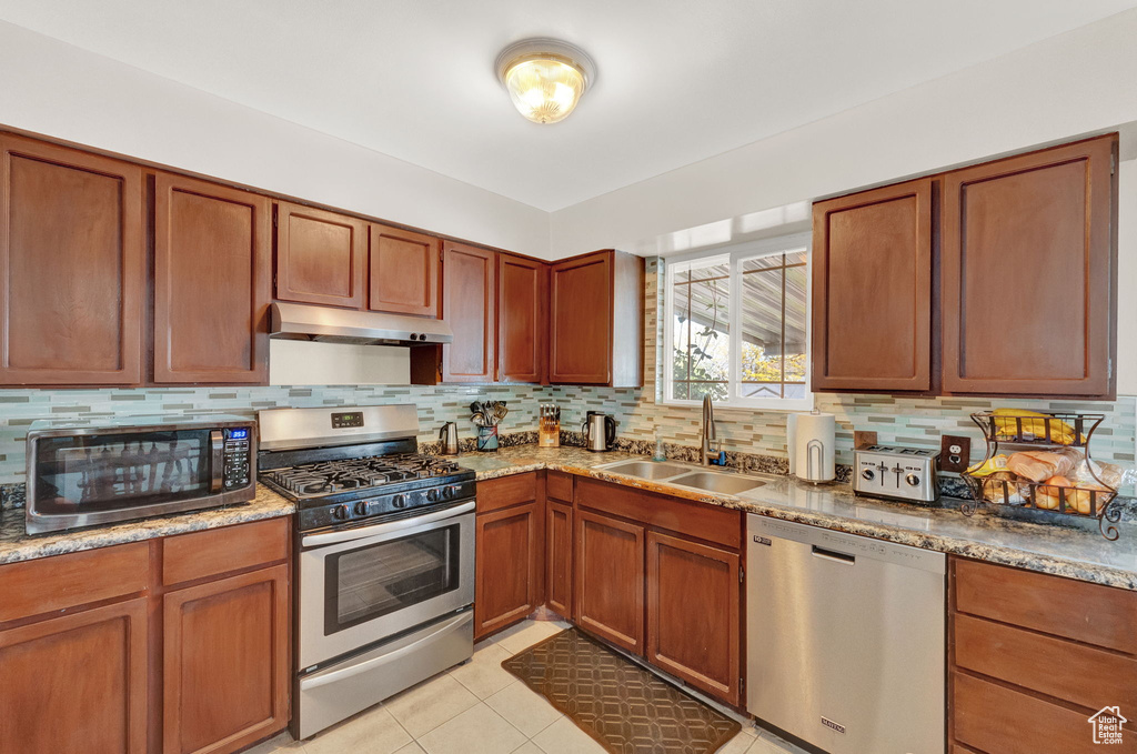 Kitchen featuring backsplash, stainless steel appliances, sink, and light tile flooring