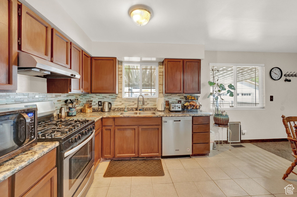 Kitchen with light stone countertops, light tile flooring, backsplash, stainless steel appliances, and sink