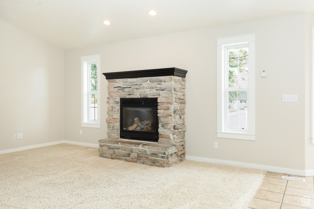 Unfurnished living room featuring a stone fireplace, tile flooring, and plenty of natural light