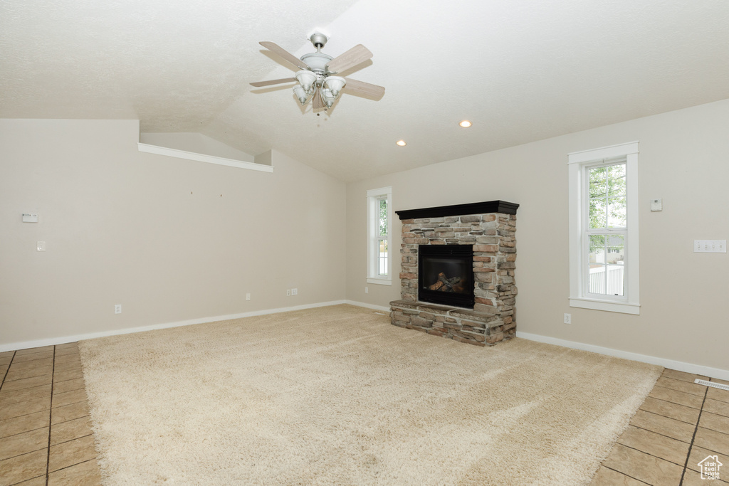 Unfurnished living room featuring vaulted ceiling, ceiling fan, light tile flooring, and a fireplace