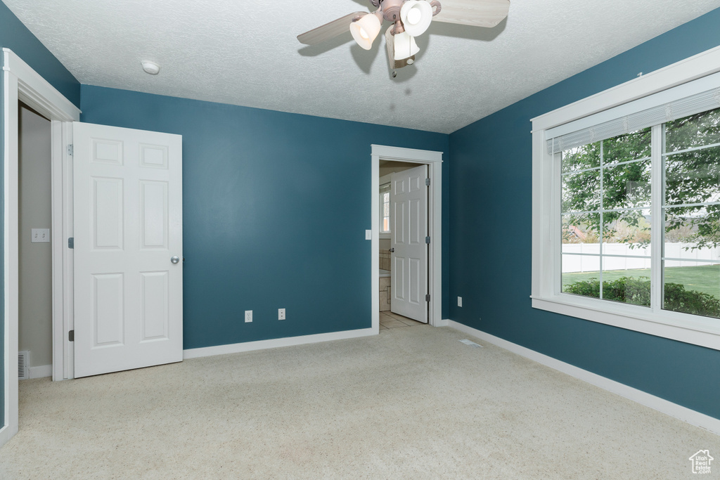 Empty room with ceiling fan, carpet flooring, a wealth of natural light, and a textured ceiling