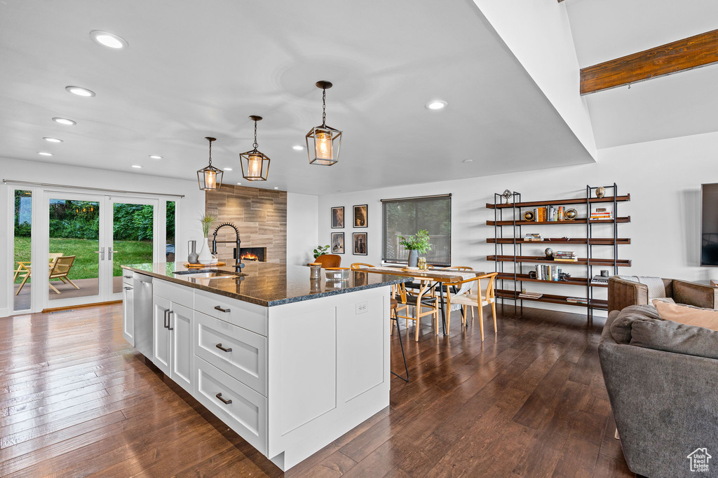 Kitchen with dark stone countertops, dark hardwood / wood-style floors, a center island with sink, and white cabinets