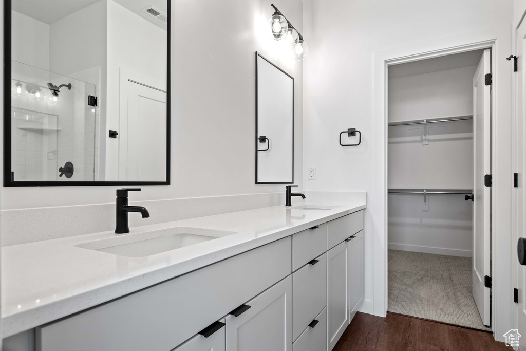 Bathroom featuring dual sinks, vanity with extensive cabinet space, hardwood / wood-style flooring, and walk in shower