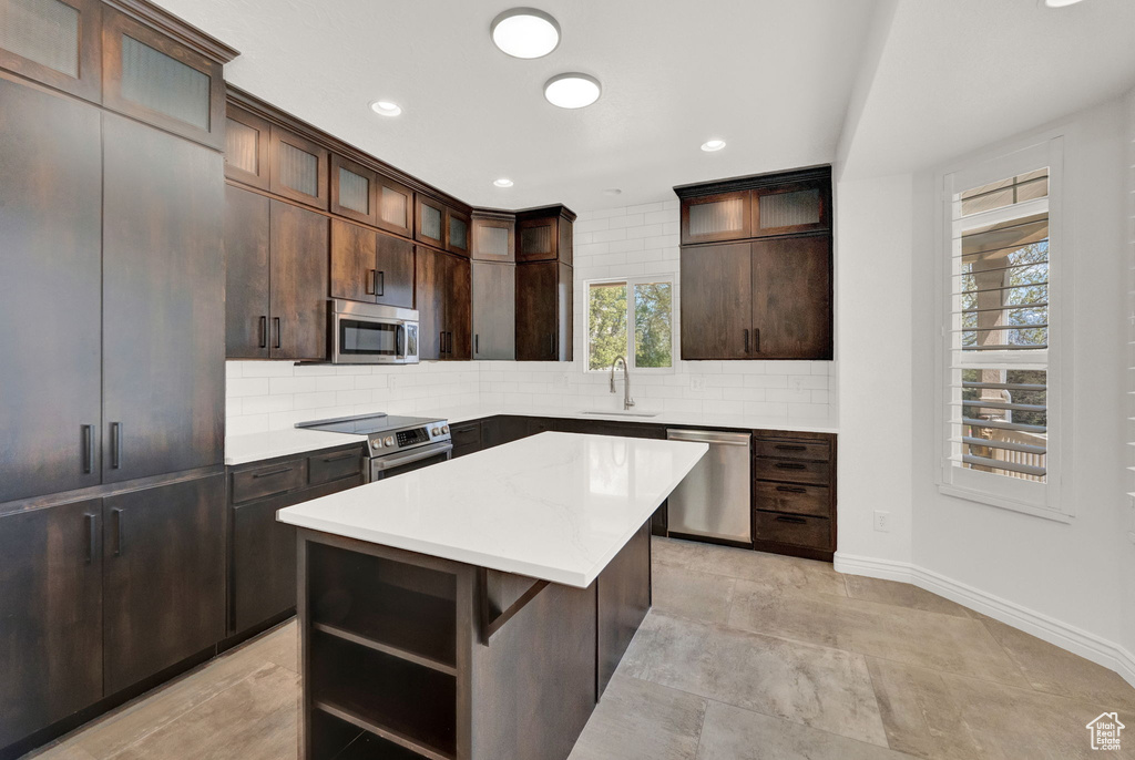 Kitchen featuring dark brown cabinets, backsplash, stainless steel appliances, sink, and a center island