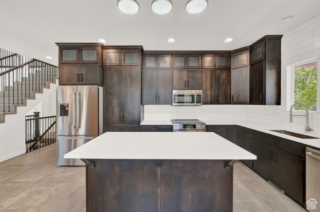 Kitchen with dark brown cabinetry, sink, high quality appliances, and a center island