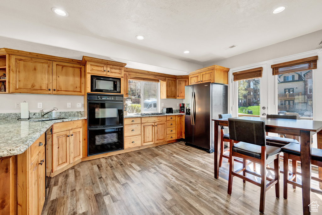 Kitchen featuring light hardwood / wood-style flooring, sink, light stone counters, and black appliances