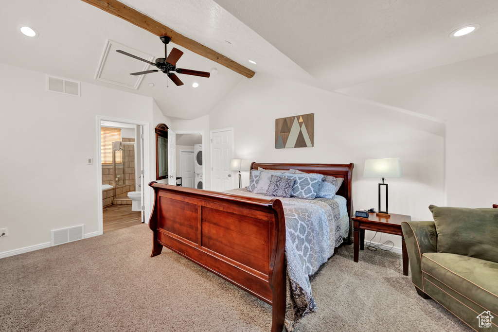 Carpeted bedroom with ceiling fan, stacked washer / dryer, lofted ceiling with beams, and ensuite bathroom