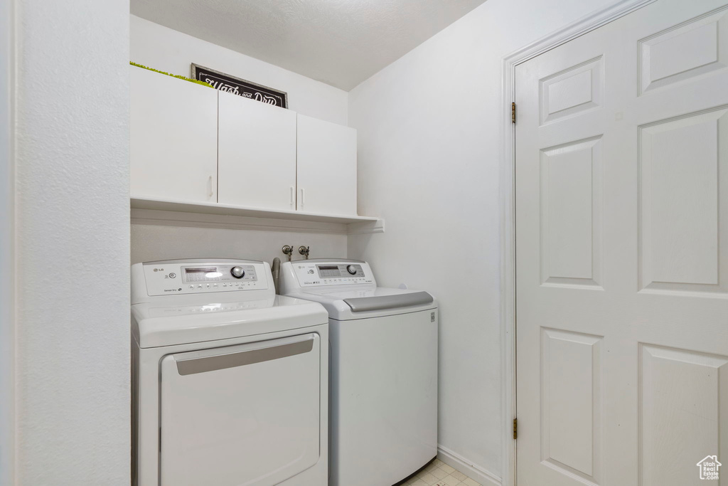 Washroom featuring cabinets, hookup for a washing machine, light tile floors, and washing machine and clothes dryer