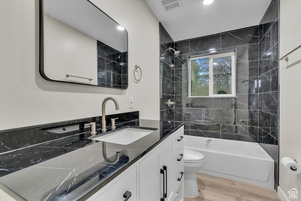 Full bathroom featuring tiled shower / bath, toilet, vanity, and hardwood / wood-style floors