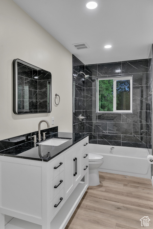 Full bathroom with wood-type flooring, vanity, toilet, and tiled shower / bath