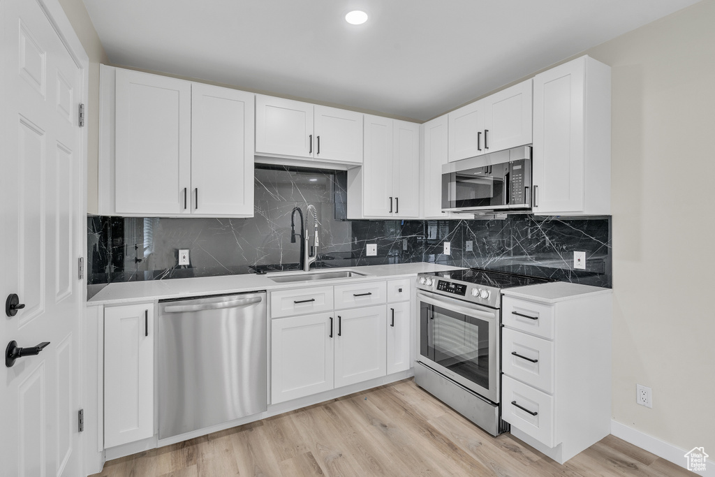 Kitchen featuring white cabinets, stainless steel appliances, sink, tasteful backsplash, and light hardwood / wood-style floors