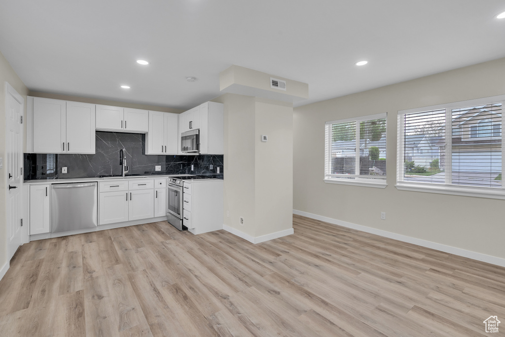 Kitchen featuring appliances with stainless steel finishes, tasteful backsplash, light hardwood / wood-style floors, and white cabinets