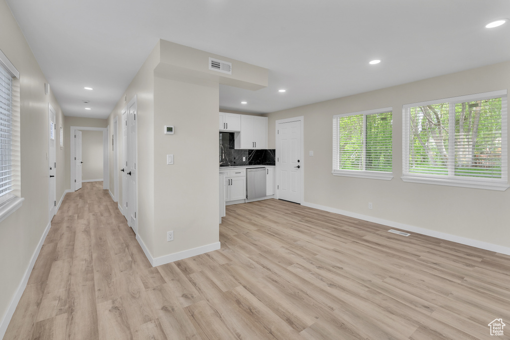 Kitchen featuring white cabinets, light hardwood / wood-style floors, backsplash, and stainless steel dishwasher